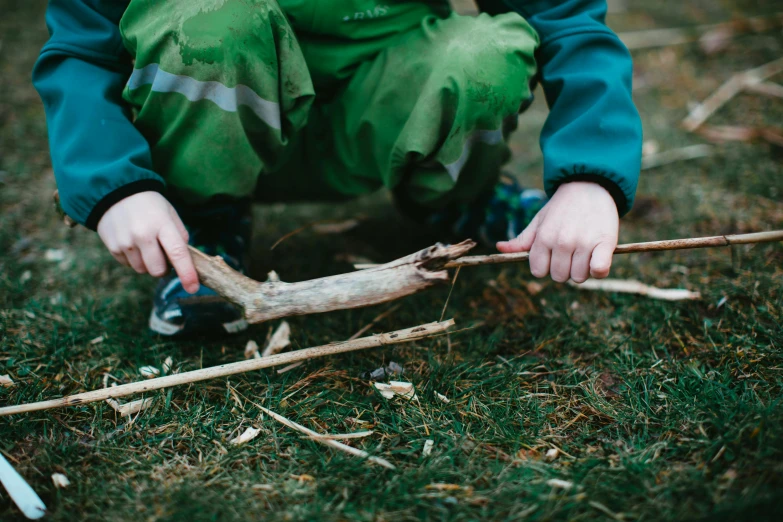 a little boy that is kneeling down in the grass, inspired by Andy Goldsworthy, unsplash, land art, holding a burning wood piece, close-up on legs, holding a crowbar, lachlan bailey