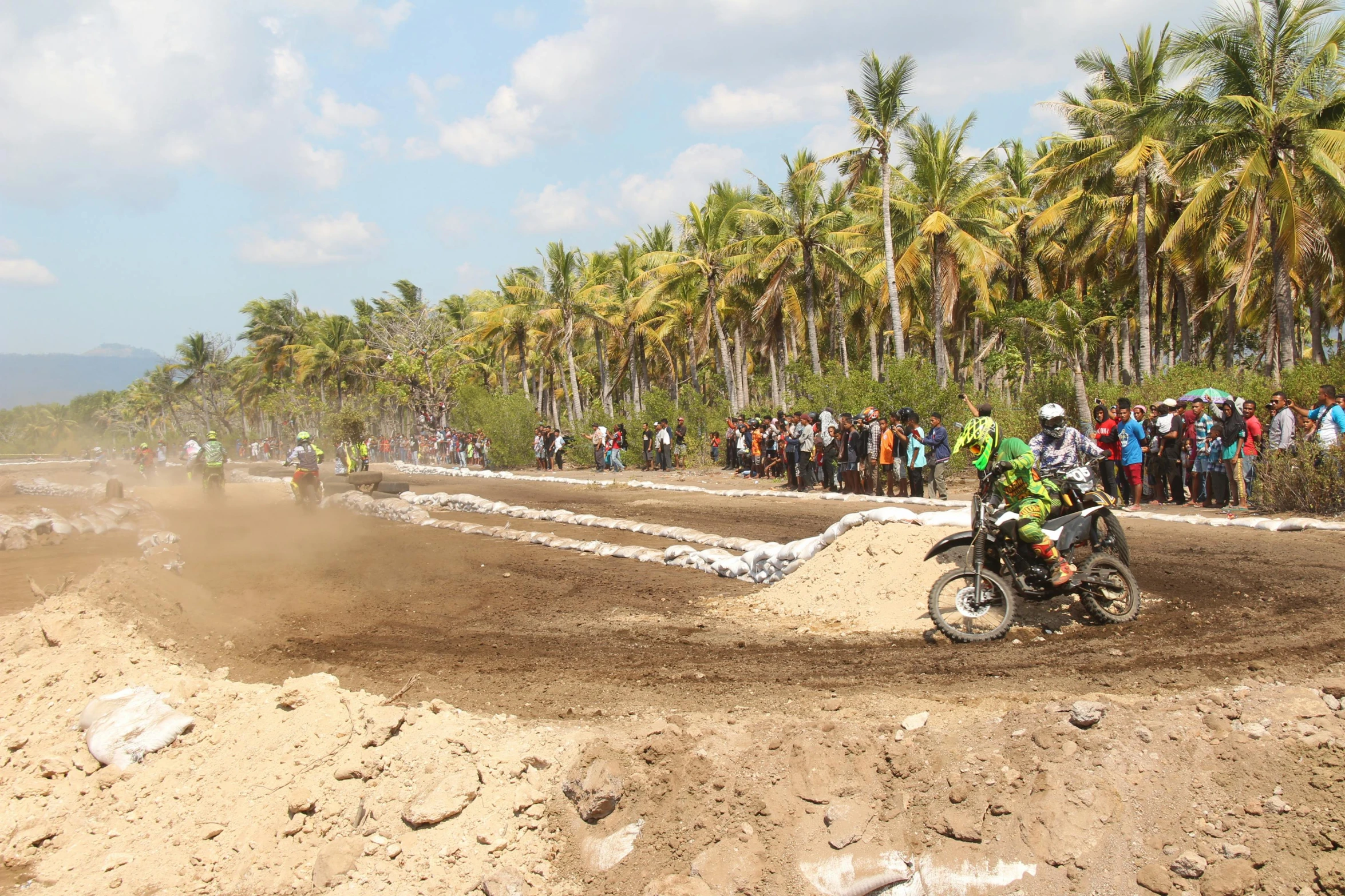 a person riding a dirt bike on a dirt track, coconut trees, crowd, gravels around, profile image