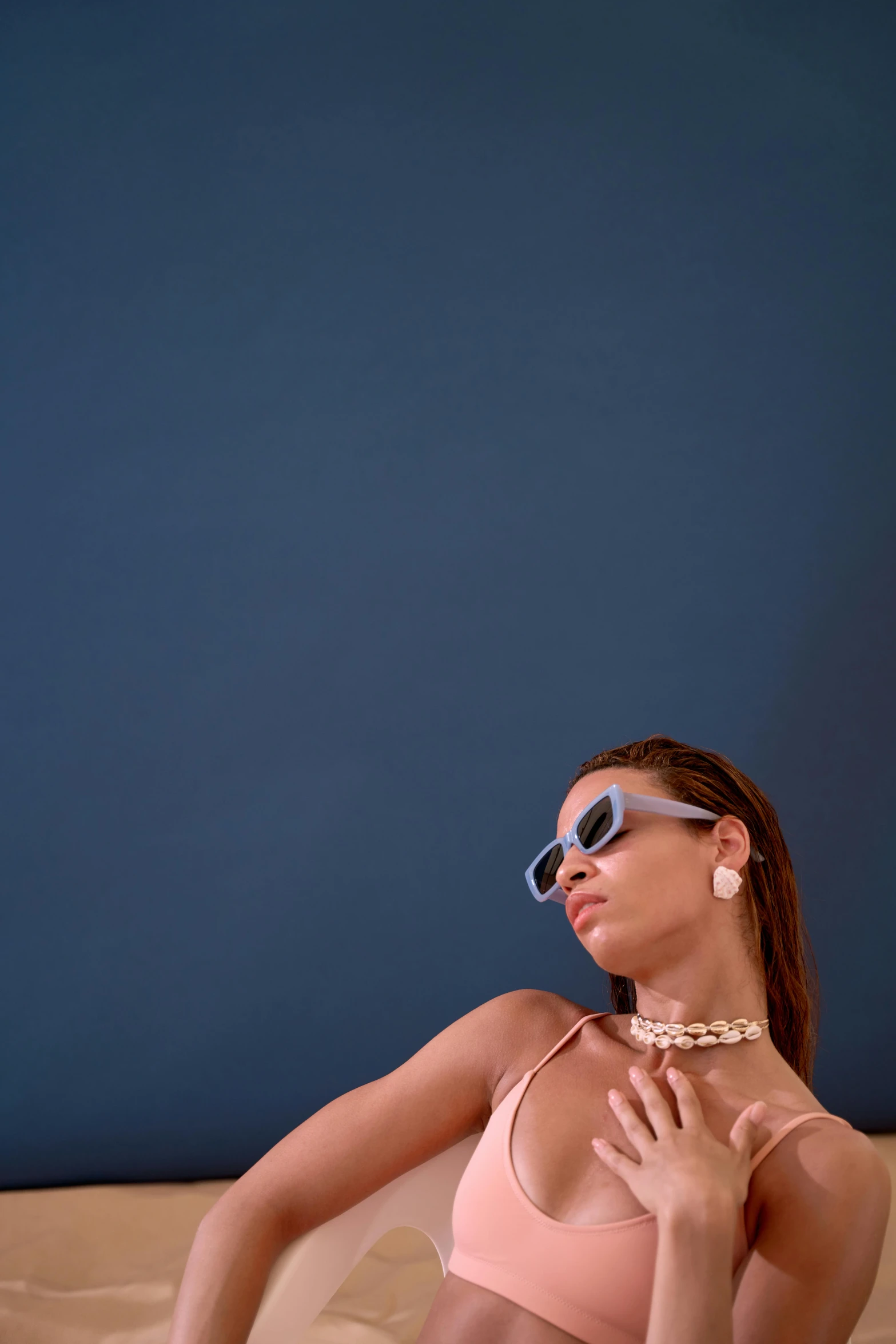 a woman in a pink bikini sitting on a bed, an album cover, trending on pexels, wearing blue sunglasses, beyonce photoshoot, cinematic shot ar 9:16 -n 6 -g, solid background