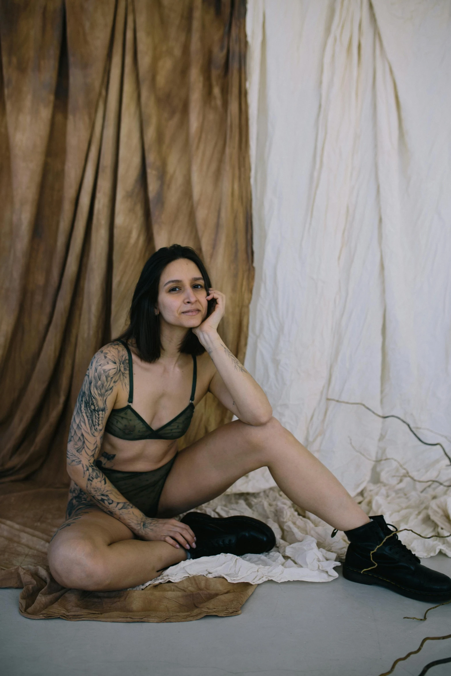 a woman sitting on the ground talking on a cell phone, a portrait, inspired by Elsa Bleda, unsplash contest winner, renaissance, black underwear, wearing camo, standing in corner of room, tattooed body