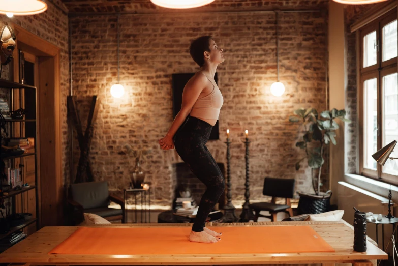 a woman standing on top of a table in a living room, pexels contest winner, arabesque, marjaryasana and bitilasana, low quality footage, brown, sacral chakra