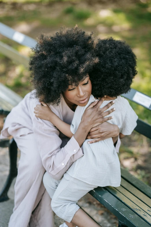 two women hugging each other on a park bench, pexels, black curly hair, young child, mother, essence