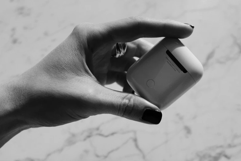 a person holding an apple airpods in their hand, a black and white photo, by Emma Andijewska, unsplash, minimalism, square, polished white marble, silicone cover, 4 k post