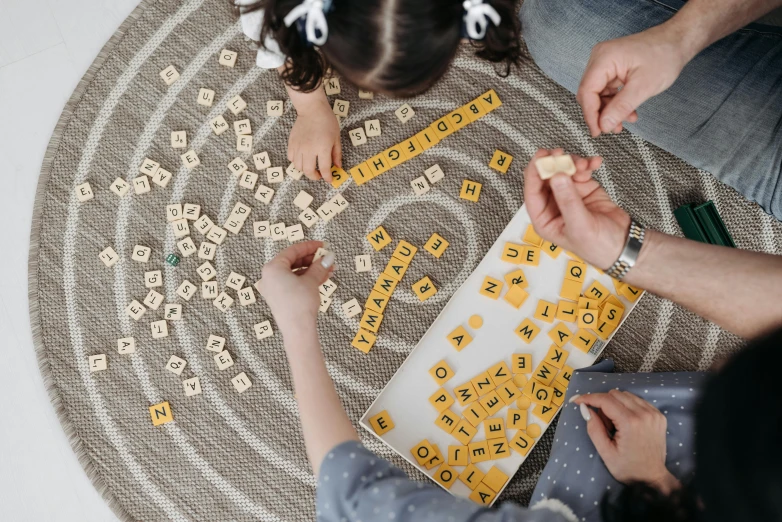 a couple of people sitting on top of a rug, by Emma Andijewska, pexels contest winner, letterism, lady using yellow dress, game board, kids, educational supplies