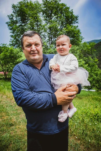 a man holding a baby in a field, by Ivan Grohar, pixabay contest winner, viktor orban in a forest, president of belorussia, in the mountains, avatar image