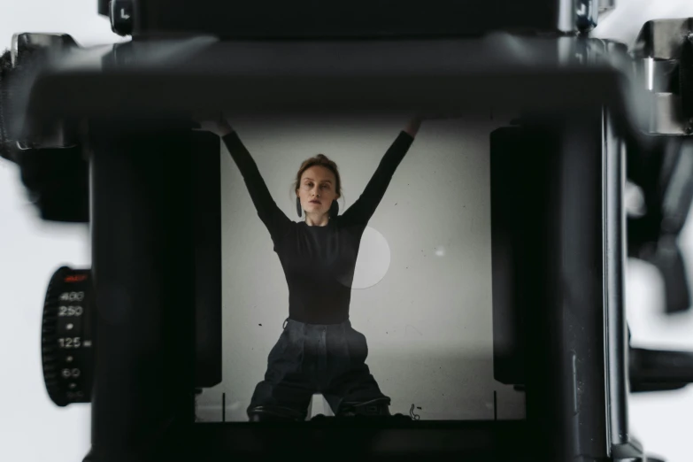 a woman that is standing in front of a camera, a hologram, inspired by Anna Füssli, unsplash, video art, large format camera, with arms up, sitting on a table, natali portman
