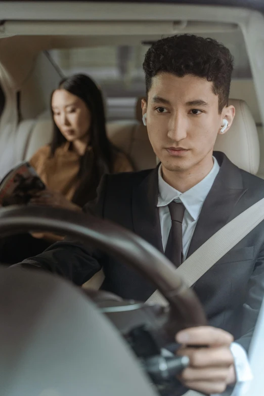 a couple of people that are sitting in a car, an album cover, inspired by Zhang Xiaogang, trending on pexels, wearing business suit, earbuds, concentrated, teenage boy