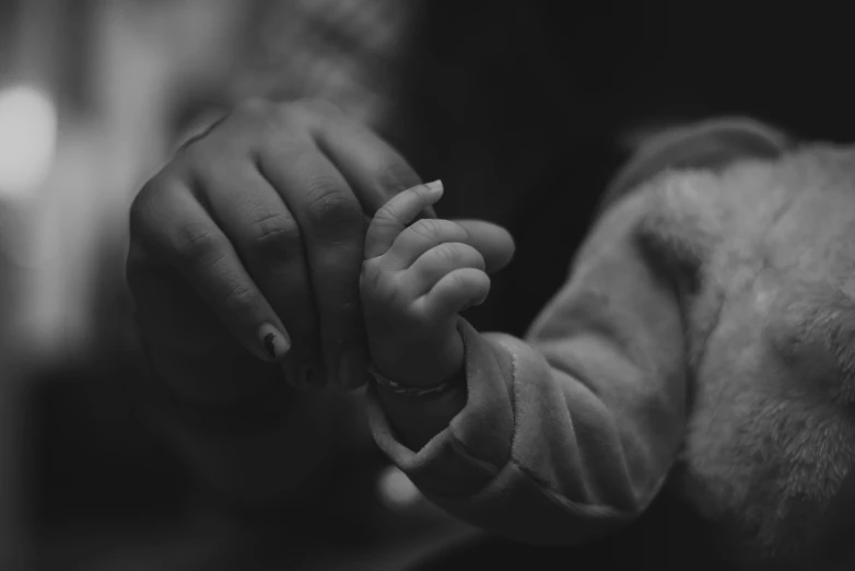 a close up of a person holding a baby's hand, a black and white photo, by Emma Andijewska, pexels, realistic footage, 8k photo, desaturated, thumbnail