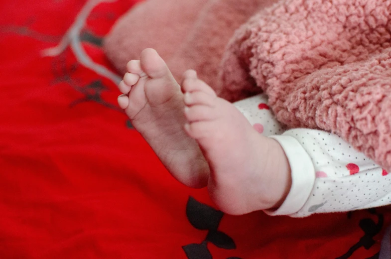 a baby laying on top of a bed next to a teddy bear, by Georgina Hunt, pexels, her hands are red roots, layed on a red velvet fabric, bare foot, detail shot