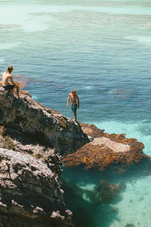 a couple of people that are sitting on some rocks, sapphire waters below, zac retz, australian, down there