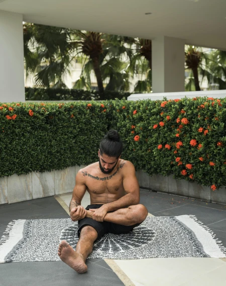 a man sitting on the ground doing a yoga pose, a tattoo, by Robbie Trevino, hurufiyya, next to a tropical pool, areas rugs, lgbtq, white bandages on fists