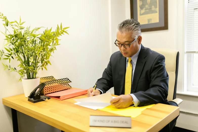 a man sitting at a desk writing on a piece of paper, shin hanga, professional profile photo, wearing a suit and glasses, hoang long ly, rafeal albuquerque