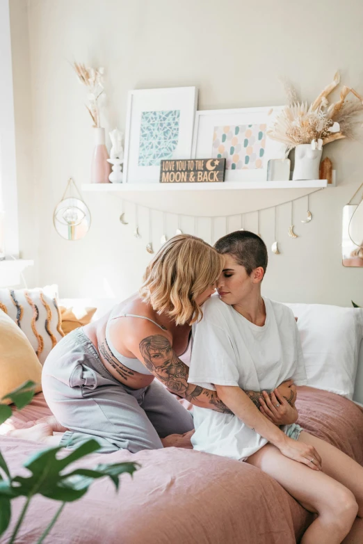 a couple of people sitting on top of a bed, by Emily Mason, trending on pexels, lesbian embrace, tattooed, mom, pastel hues