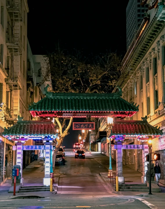 a street filled with lots of traffic next to tall buildings, a photo, trending on unsplash, art nouveau, chinatown bar, large gate, at nighttime, lgbtq