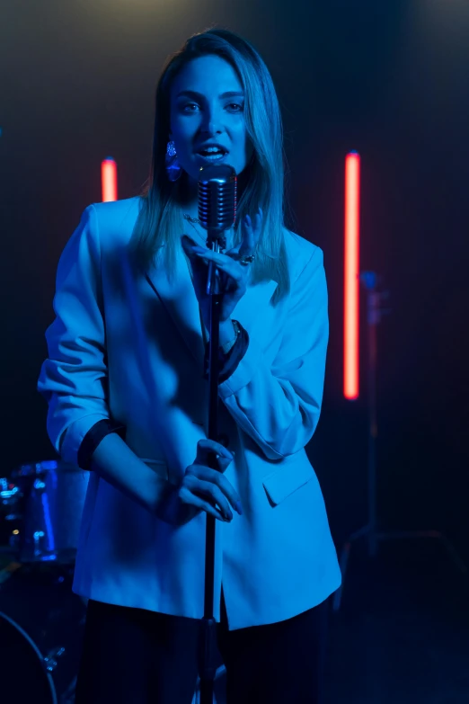 a woman standing in front of a microphone, an album cover, inspired by Elsa Bleda, pexels, girl in suit, performing a music video, blue light, band