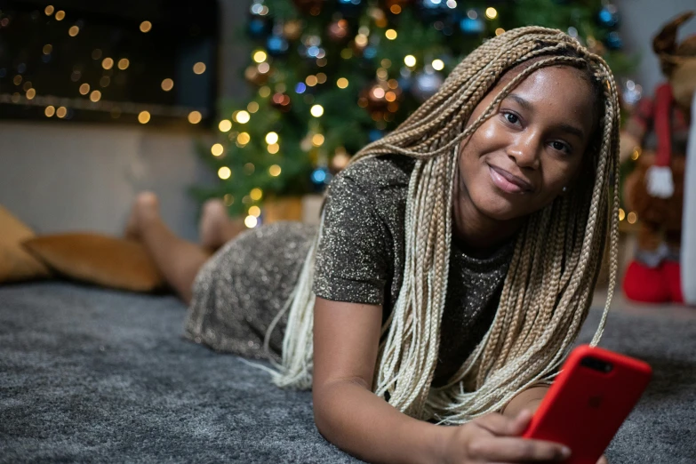 a young girl laying on the floor in front of a christmas tree, a portrait, pexels contest winner, happening, black teenage girl, using a magical tablet, smiling young woman, girl with plaits