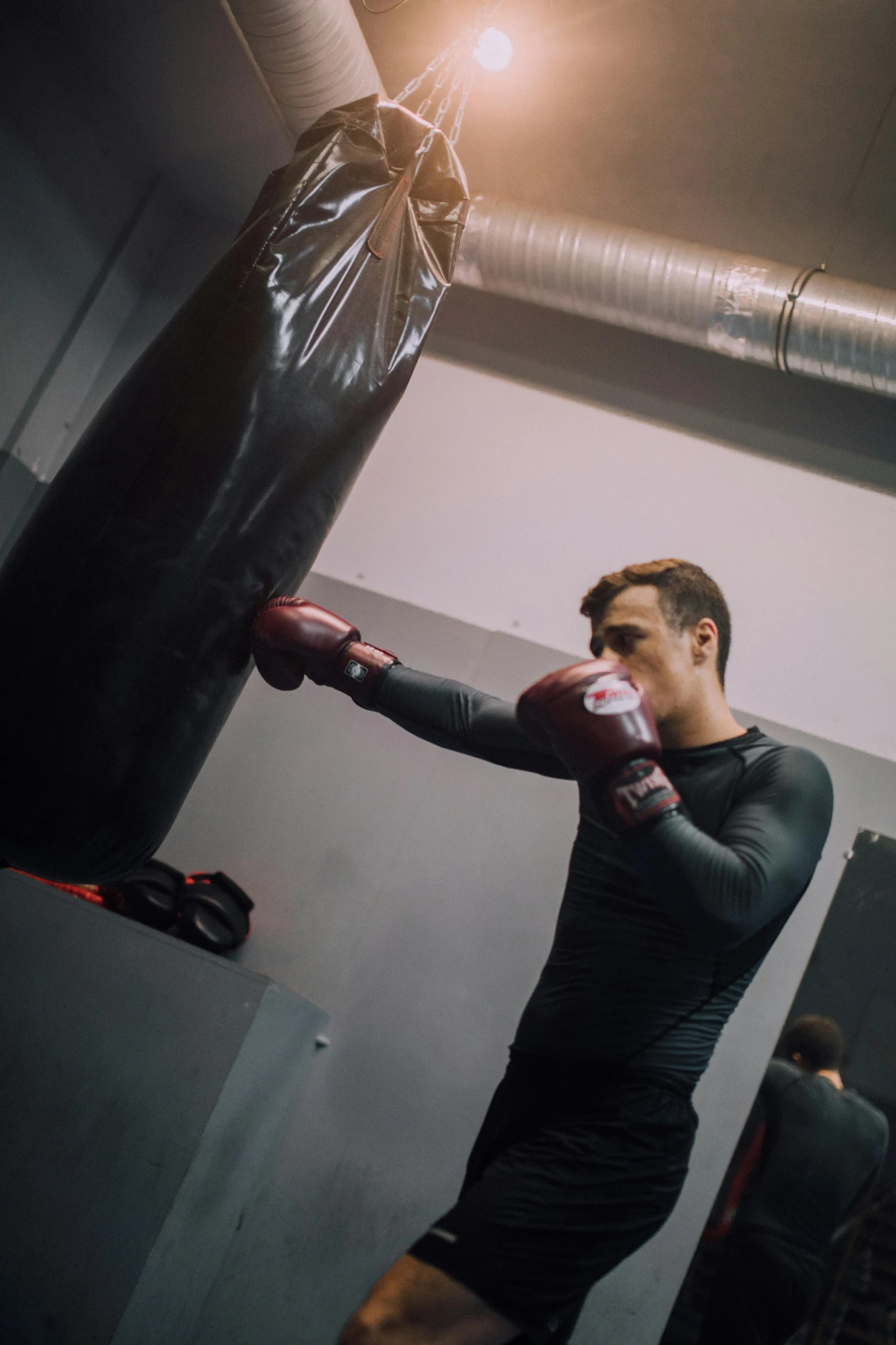 a man standing next to a punching bag, happening, black undersuit, liam, concentration, performance