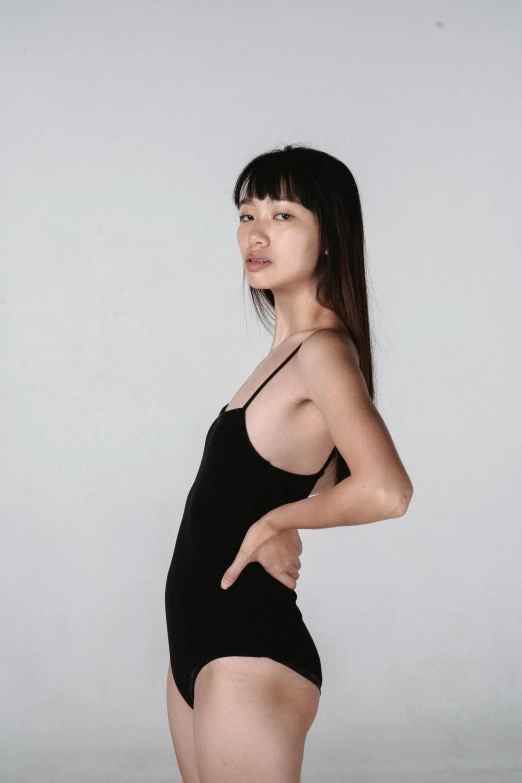 a woman in a black bodysuit posing for a picture, inspired by Wang E, reddit, in front of white back drop, wearing : tanktop, gongbi, looking from side