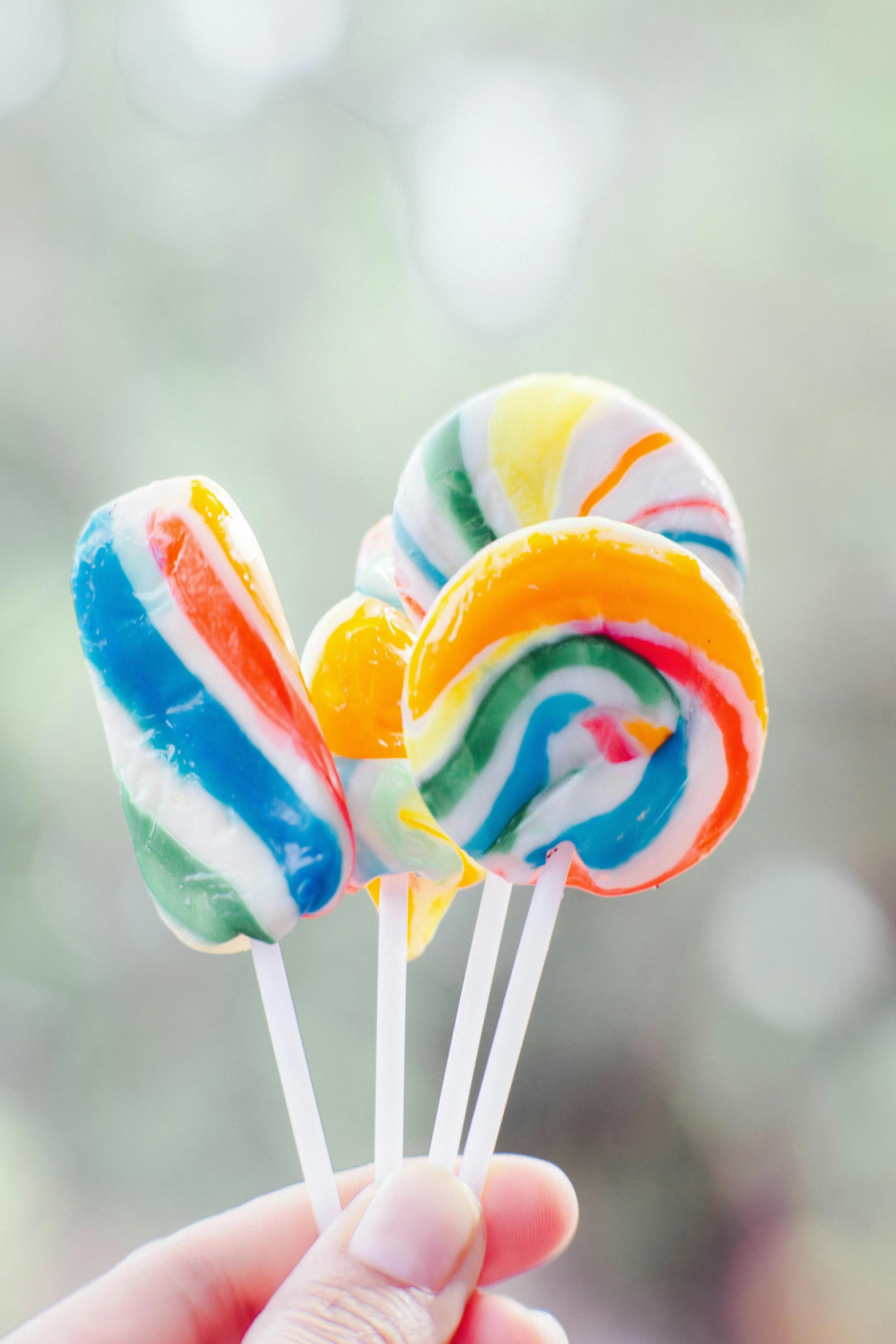 a person holding three lollipops in their hands, inspired by Jeff Koons, unsplash, colorful swirls of paint, edible, striped, sugar