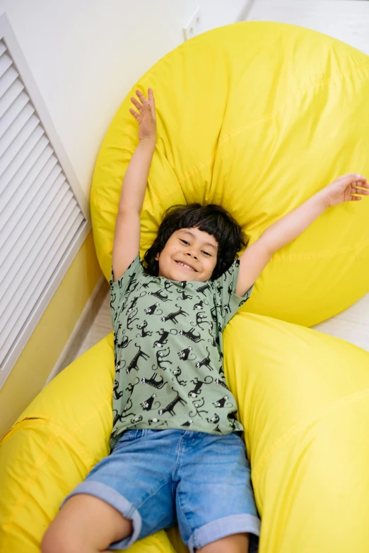 a young boy laying on a yellow bean bag chair, by Nina Hamnett, square, full device, premium quality, air shot