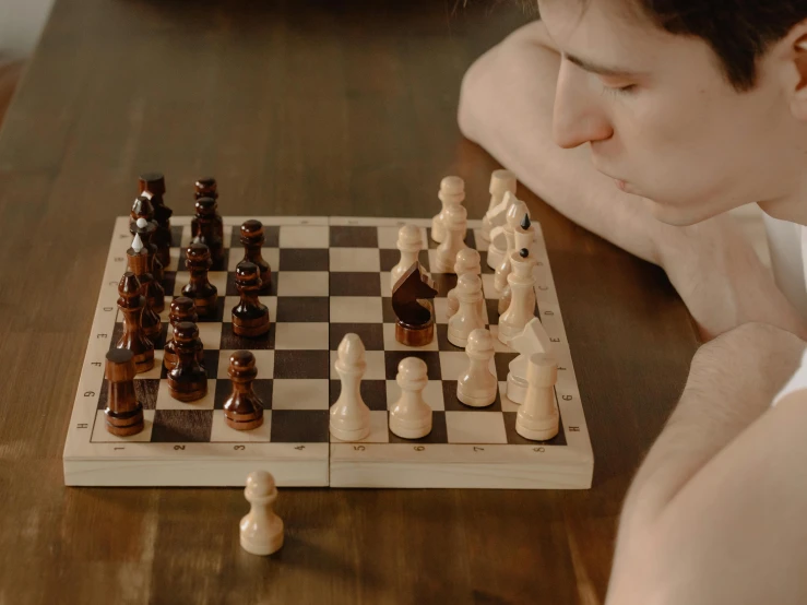 a man sitting at a table playing a game of chess, a picture, by Emma Andijewska, pexels contest winner, extremely pale white skin, sitting on a mocha-colored table, youtube thumbnail, resting after a hard fight