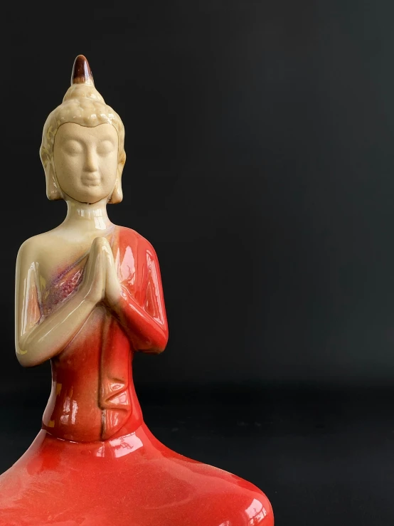 a red buddha figurine sitting on a black surface, a statue, by Glennray Tutor, 1960s, medium