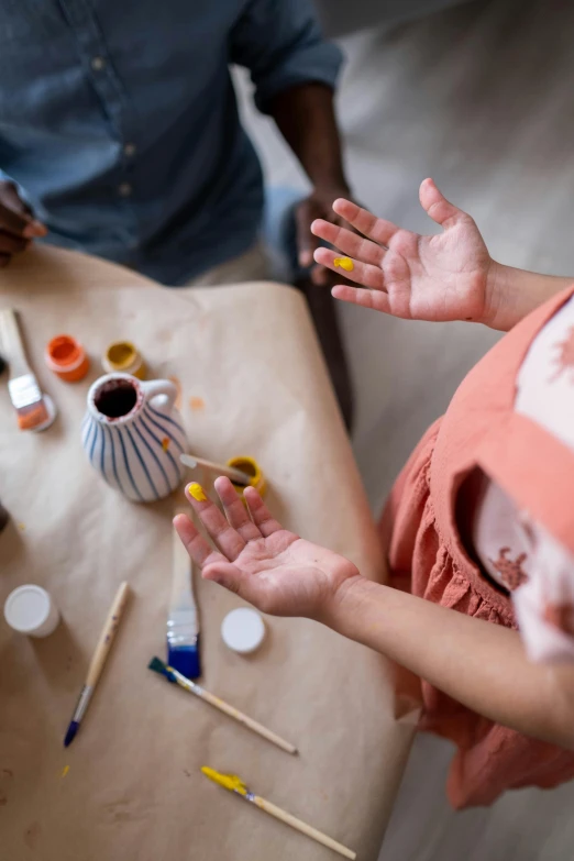 a group of people that are standing around a table, trending on pexels, process art, partially cupping her hands, can of paint, ochre, family friendly