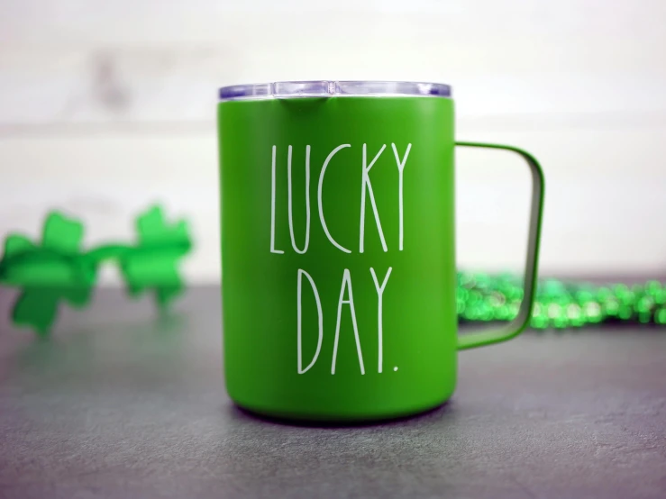 a green mug with the words lucky day on it, engraved, medium close up, on a gray background, exterior shot