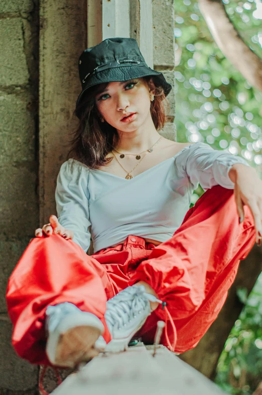 a woman sitting on a ledge next to a tree, a picture, unsplash, renaissance, baggy clothing and hat, red shirt brown pants, model エリサヘス s from acquamodels, resembling a mix of grimes