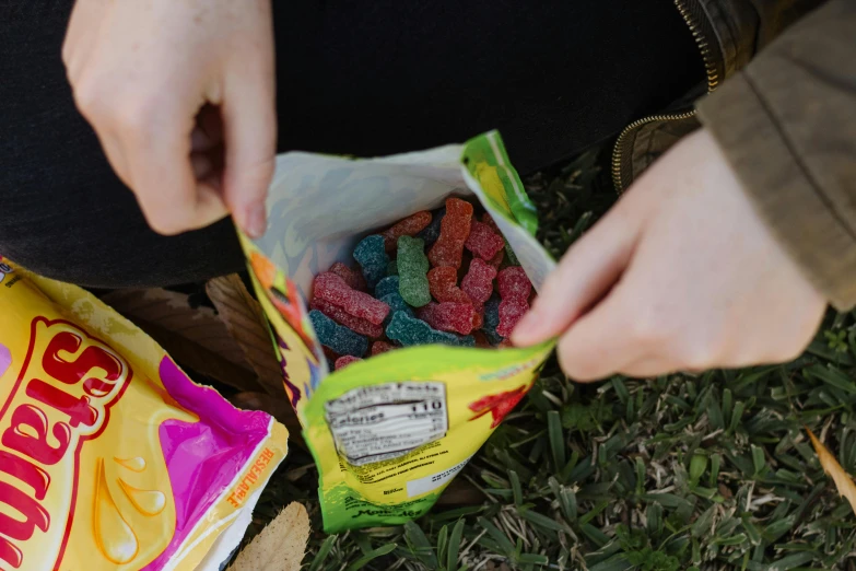 a person sitting in the grass with a bag of gummy bears, candy worms, close-up shot from behind, instagram post, having a snack