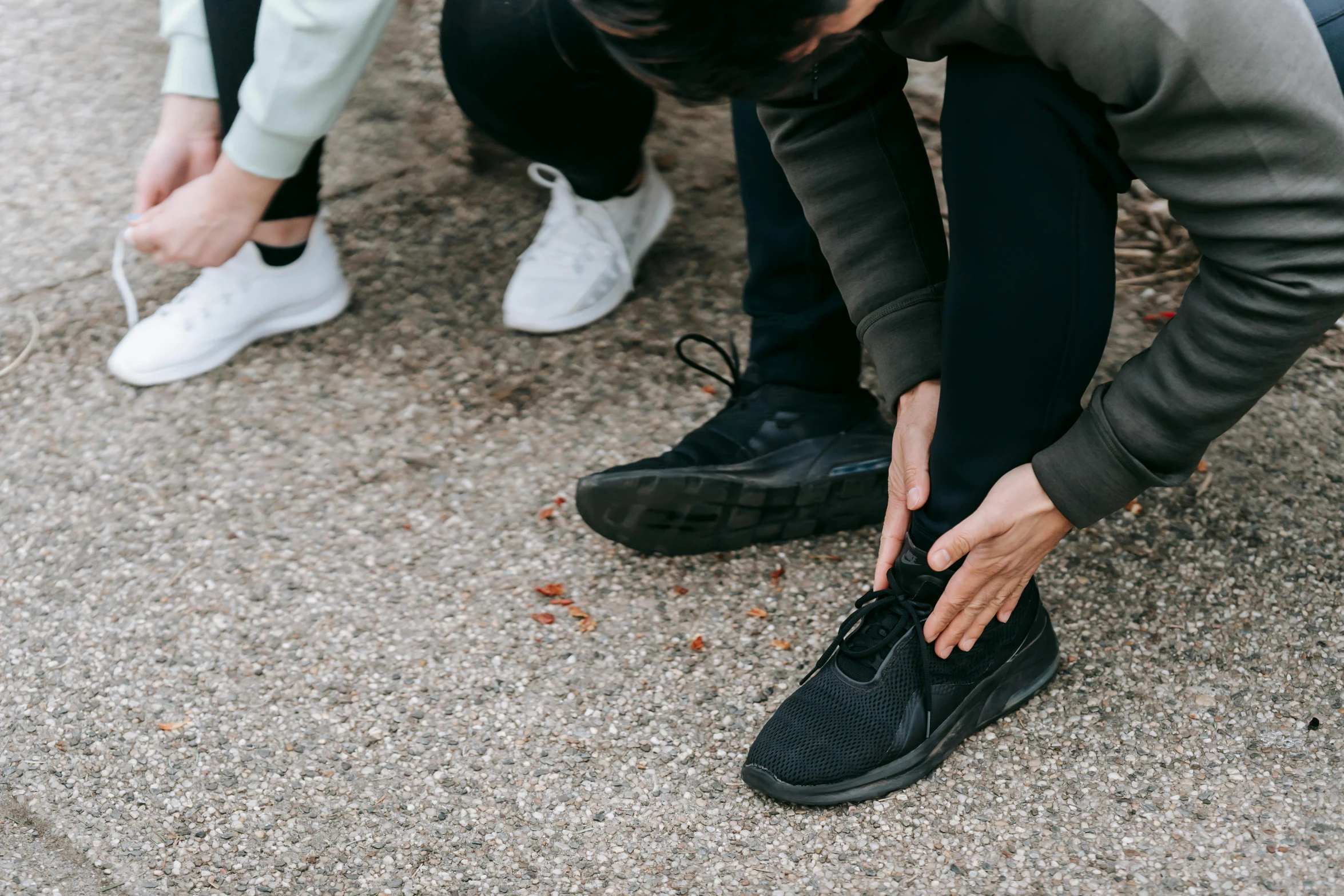 two people sitting on a bench tying up their shoes, pexels contest winner, standing on rocky ground, running shoes, grey pants and black dress shoes, swoosh