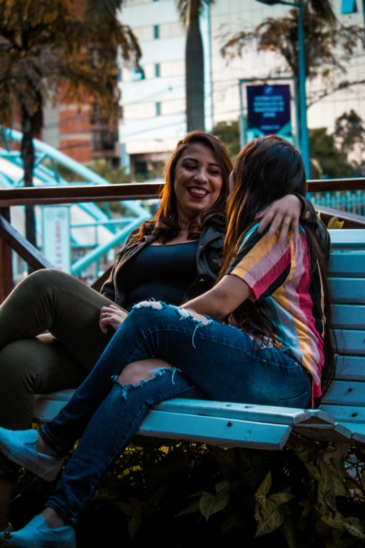 a couple of women sitting on top of a blue bench, a picture, trending on pexels, chilean, lesbian embrace, wearing casual clothing, candid