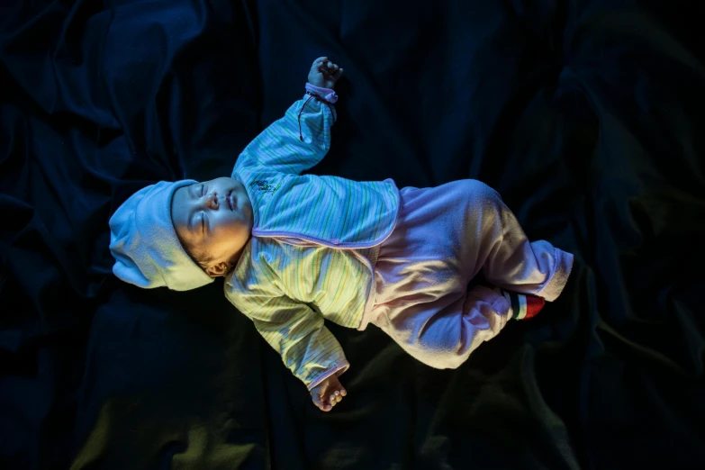 a baby laying on top of a black sheet, unsplash, hyperrealism, glowing with colored light, high angle, future activist, lights off