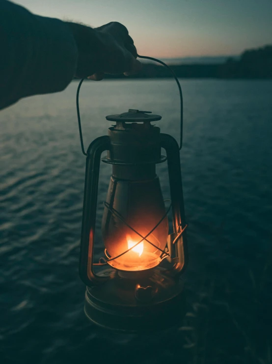 a person holding a lantern over a body of water, muted lighting, candle lit, instagram post, vintage glow