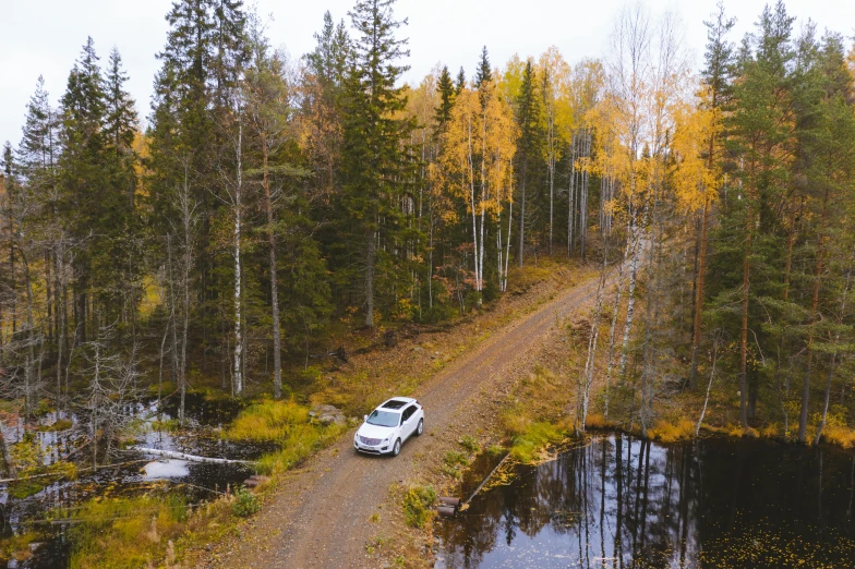 a car driving down a dirt road next to a forest, by Jaakko Mattila, pexels contest winner, hurufiyya, build in a forest near of a lake, autum, 2 5 6 x 2 5 6 pixels, wide high angle view