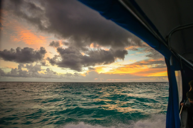 a person on a boat looking out at the ocean, happening, sunset with cloudy skies, mariana trench, turquoise water, violent stormy waters