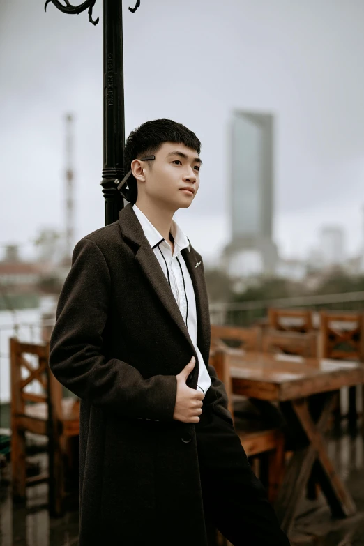 a man in a black coat standing next to a lamp post, an album cover, inspired by Ruth Jên, ((portrait)), 1 6 years old, hoang lap, at the terrace