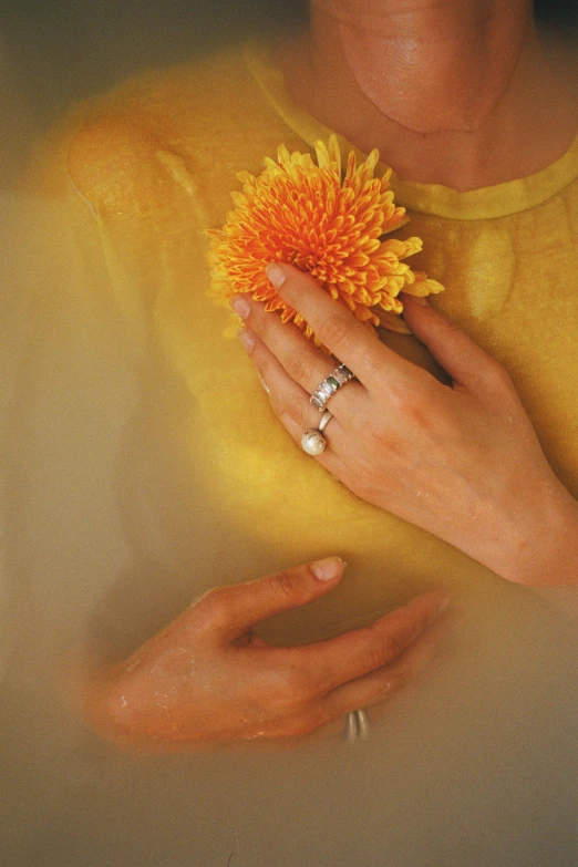 a woman holding a yellow flower in her hands, inspired by Elsa Bleda, jewelry pearls, silver，ivory, overhead sun, bath