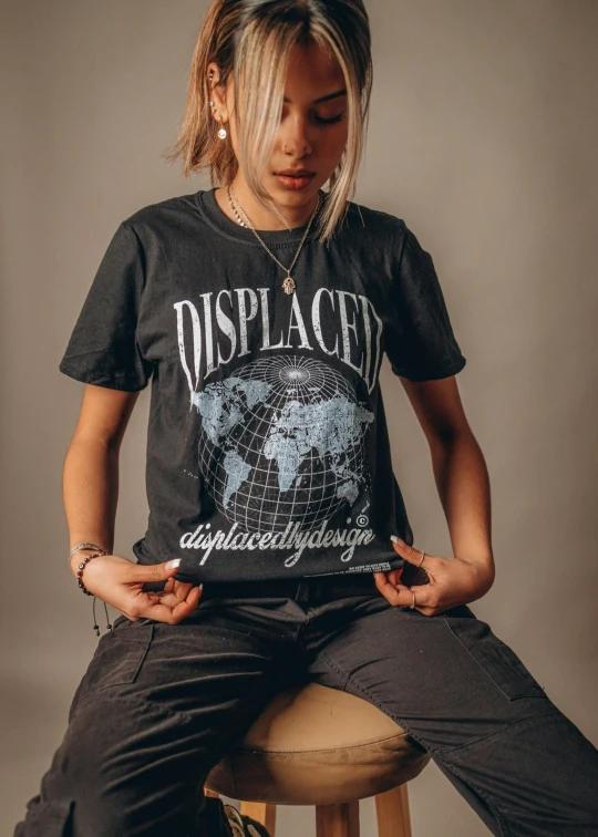 a woman sitting on a stool with her hands in her pockets, an album cover, inspired by Elsa Bleda, trending on unsplash, graffiti, dirty short sleeved shirt, displacement map, dark grey, deserted planet