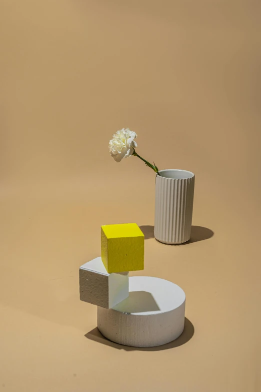 a vase sitting on top of a table next to a flower, an abstract sculpture, inspired by Giorgio Morandi, de stijl, gradient light yellow, structure : kyle lambert, high angle, blocks