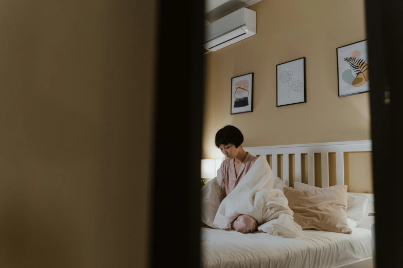 a woman sitting on top of a bed covered in a blanket, pexels contest winner, standing in corner of room, tiny person watching, asian female, background image