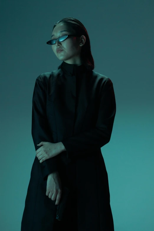 a woman in a black coat and glasses, inspired by Tadashi Nakayama, unsplash, conceptual art, japan. volumetric lighting, ao dai, ambient teal light, integrated synthetic android