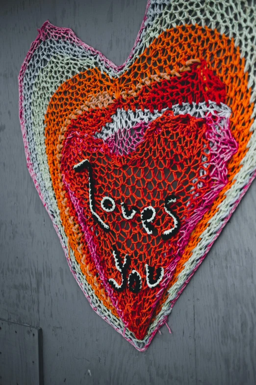 a crocheted heart hanging on a wall, by Andrée Ruellan, pexels, process art, detailed string text, knitted mesh material, the lovers, you