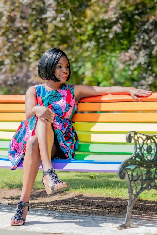 a woman sitting on a colorful bench in a park, inspired by Chinwe Chukwuogo-Roy, pexels contest winner, happening, plethora of colors ; mini dress, prideful look, multi - coloured, ebony