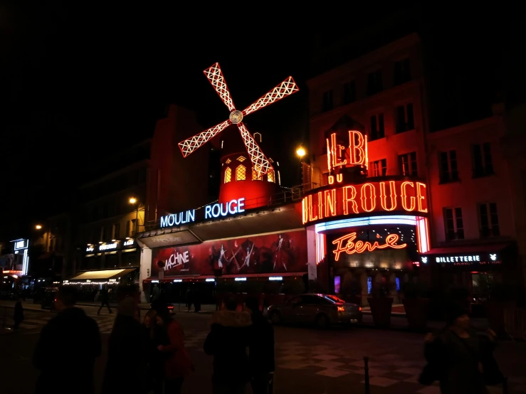 a group of people walking down a street at night, moulin rouge, in front of a black background, square, exterior photo