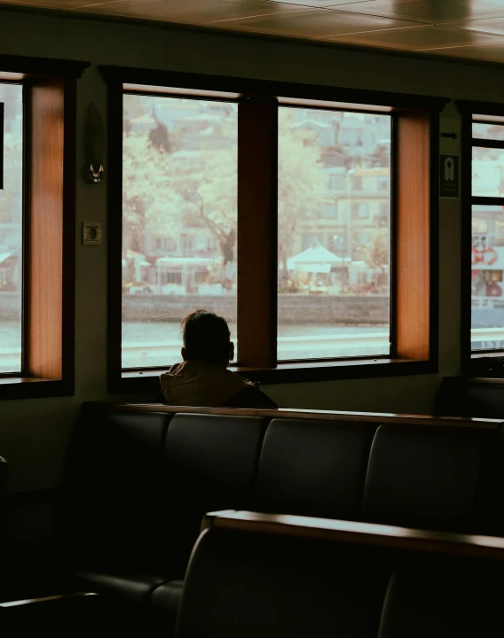 a person sitting in a chair looking out a window, a picture, inspired by Elsa Bleda, trending on unsplash, on a boat, train station, taken in the late 2010s, bars on the windows