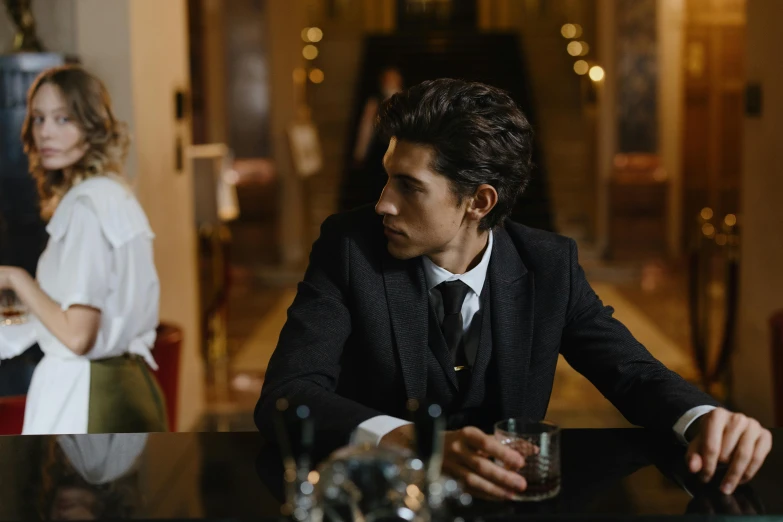 a man in a suit sitting at a bar, by Emma Andijewska, pexels contest winner, renaissance, timothee chalamet, adam driver, [ theatrical ], romance