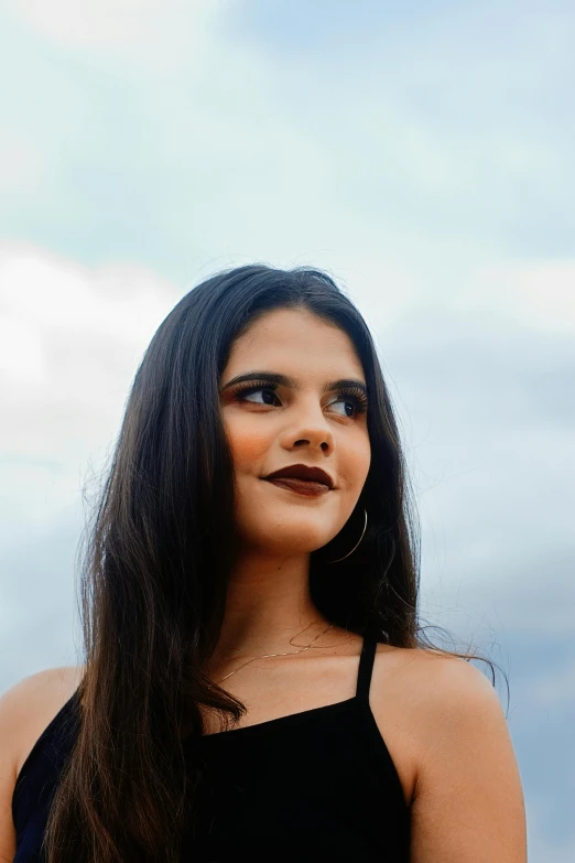 a woman in a black dress posing for a picture, by reyna rochin, pexels contest winner, dark brown hair and tan skin, 1 6 years old, skies, justina blakeney