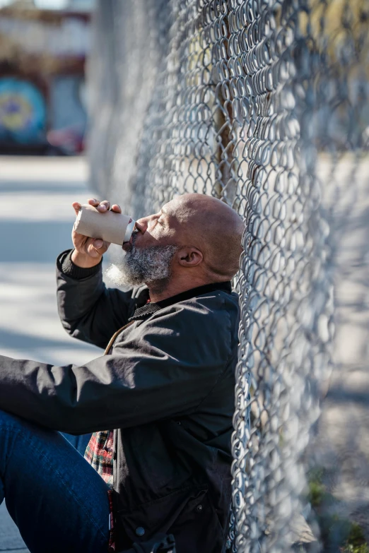 a man sitting on the sidewalk drinking from a cup, by Steve Brodner, pexels contest winner, rusty chain fencing, bald head and white beard, samuel l jackson, in a prison cell