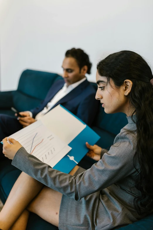 a woman sitting on a couch reading a book, a cartoon, pexels contest winner, business meeting, young middle eastern woman, wearing a pinstripe suit, two people